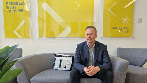 A person in a suit is sitting on a gray couch in front of three yellow posters.